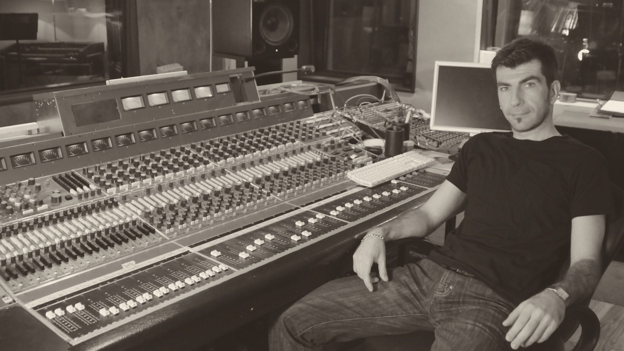 Haig V. seated beside a large mixing console in a studio, looking into the camera.