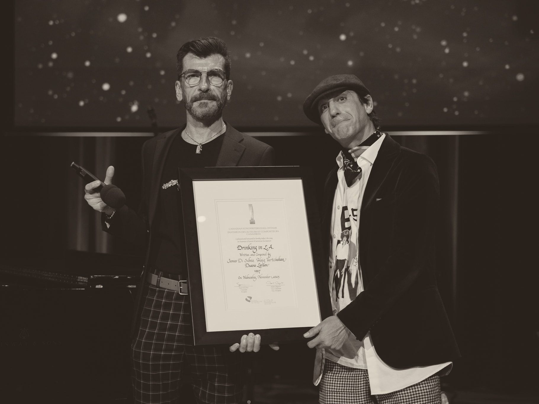 Haig V. and James Di Salvio on a stage, holding the framed Canadian Songwriters Hall of Fame certificate for “Drinking in L.A.”.